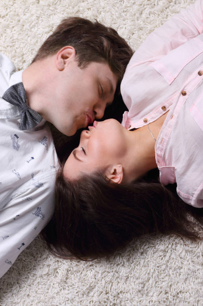 Happy woman and young man in bow tie kiss on carpet, top view - Photo, image