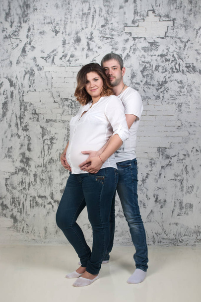 Young pretty pregnant woman and man in jeans poses in white stud - 写真・画像
