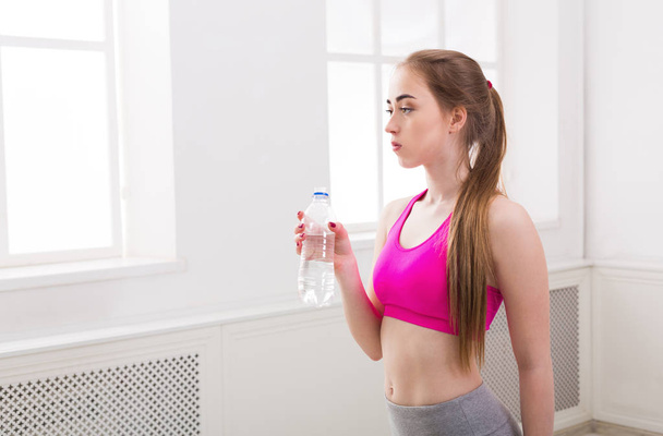 Fitness-Frau trinkt Wasser im Fitnessstudio auf weißem Hintergrund - Foto, Bild