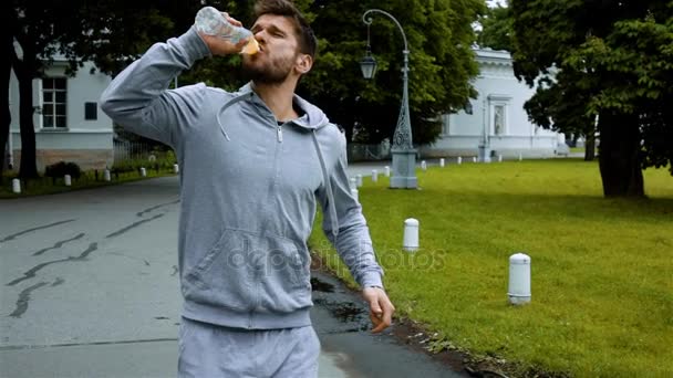 Sportovec pít čistou vodu z láhve stříkající vodou. - Záběry, video