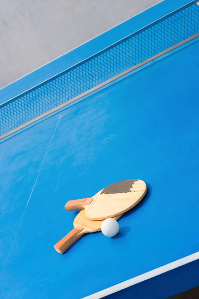 старые ракетки для пинг-понга и мяч и сетка на синем столе для пинг-понга
 - Фото, изображение
