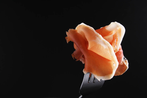 prosciutto, jamon on a fork a dark background - Photo, image