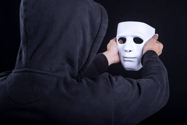 Таинственный человек держит и смотрит на белую маску
 - Фото, изображение