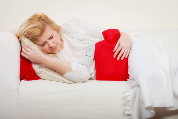 Woman feeling stomach cramps lying on cofa - Photo, image