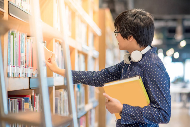 Joven asiático hombre estudiante elegir libro en biblioteca
 - Foto, imagen