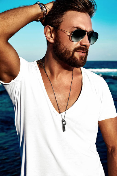 Portrait of handsome fashion man model wearing white clothes posing on blue sea background - Fotografie, Obrázek
