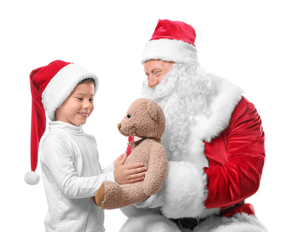 白い背景の上のクリスマス帽子かわいい男の子にテディベアを与える本物のサンタ クロース - 写真・画像