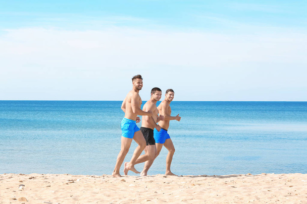 Handsome young men running along sea beach - Photo, Image