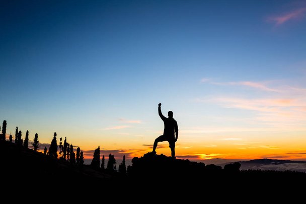 Ο άνθρωπος γιορτάζει ηλιοβασίλεμα στα βουνά με τα όπλα τεντωμένος - Φωτογραφία, εικόνα