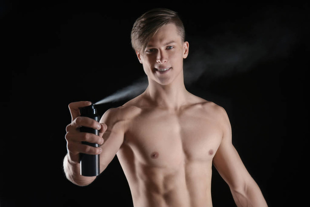 Handsome young man with deodorant on dark background - Фото, изображение