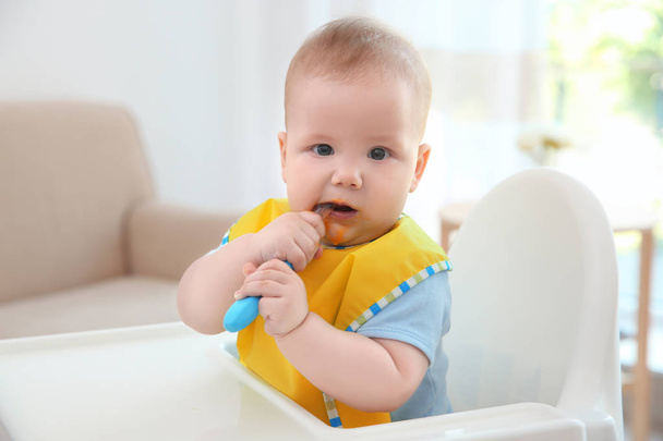 Cute baby with spoon sitting in kitchen - Valokuva, kuva