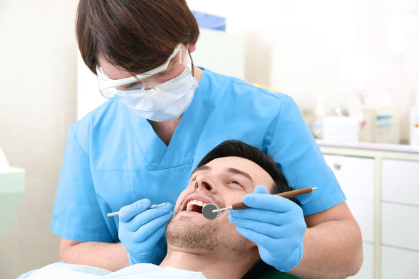Dentist examining man's teeth in clinic - Foto, imagen