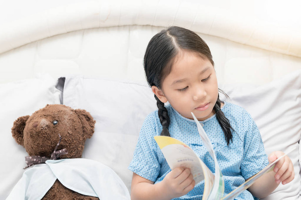 cute little asian girl reading fairy tales book on bed - Fotó, kép