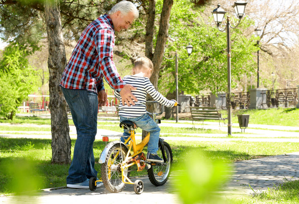 Cute little boy riding on bicycle and his grandfather in spring park - Fotó, kép