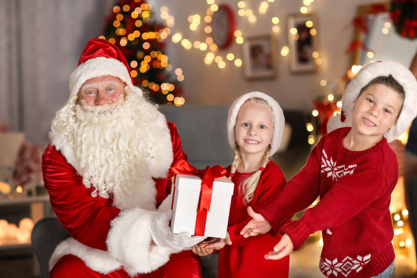 Santa Claus giving present to children in room with beautiful Christmas decorations - Foto, Imagen