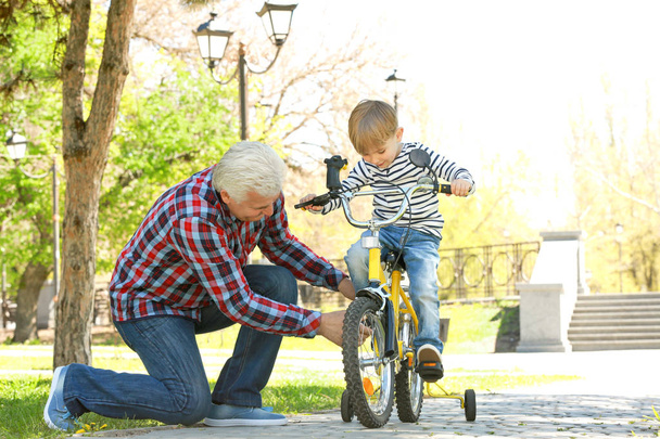 Cute little boy riding on bicycle and his grandfather in spring park - Fotó, kép