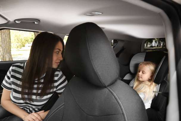 Young woman looking at small girl in safety seat inside of car - Photo, Image