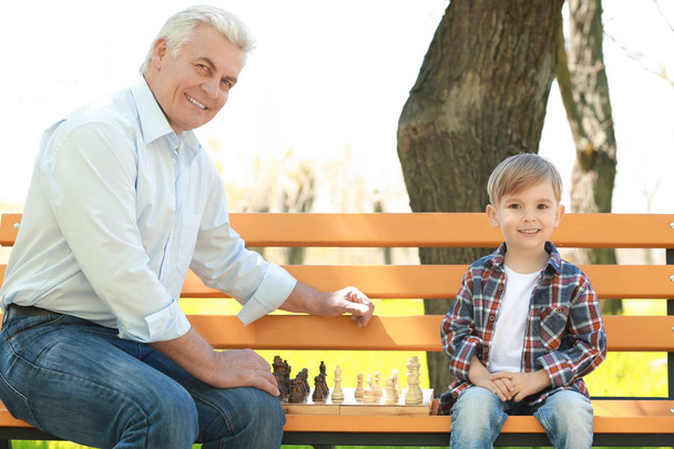 Menino bonito com seu avô jogando xadrez no banco no parque de primavera
 - Foto, Imagem