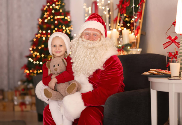 Santa Claus and cute little girl with toy in room decorated for Christmas - Photo, Image