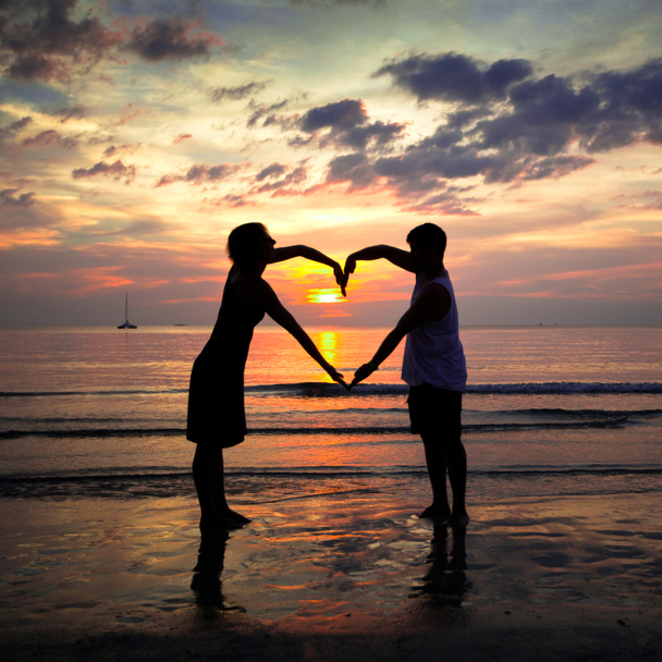 νεαρό ζευγάρι, κρατώντας τα χέρια, καρδιά-διαμορφωμένα στην παραλία θάλασσα στο ηλιοβασίλεμα - Φωτογραφία, εικόνα