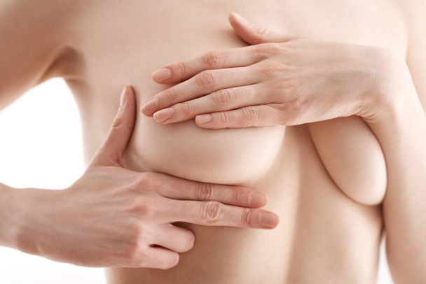 Women's health. Close up of a young nude woman touching her chestbreast and rising breast cancer awareness while standing isolated on white background - Photo, Image