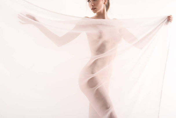 Αθώα ομορφιά. Ελκυστική νεαρή γυναίκα γυμνό καλύπτοντας με ένα τούλι και να στέκεται πάνω σε λευκό φόντο και αίσθηση υγιή - Φωτογραφία, εικόνα