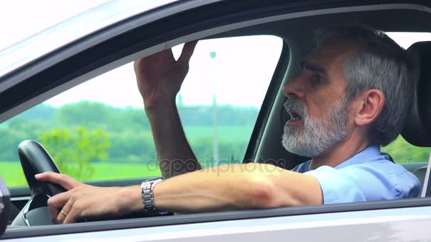 Старший сидит в машине и жалуется на дорожную ситуацию - крупный план со стороны - сельская местность на заднем плане
 - Кадры, видео