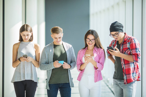 τέσσερις φίλοι που εργάζονται στην εταιρεία να εθιστεί από gadgets, χρησιμοποιώντας έξυπνα τηλέφωνα και tablet για την αναζήτηση κοινωνικών δικτύων και την ανταλλαγή μηνυμάτων με τους φίλους σε απευθείας σύνδεση - Φωτογραφία, εικόνα