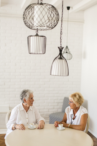 Kaksi vanhempaa naista juomassa kahvia kotona ja puhumassa
 - Valokuva, kuva