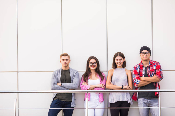 Gruppo di quattro giovani sorridenti che indossano abiti casual alla moda guardando la fotocamera in piedi in ufficio leggero o all'università
. - Foto, immagini