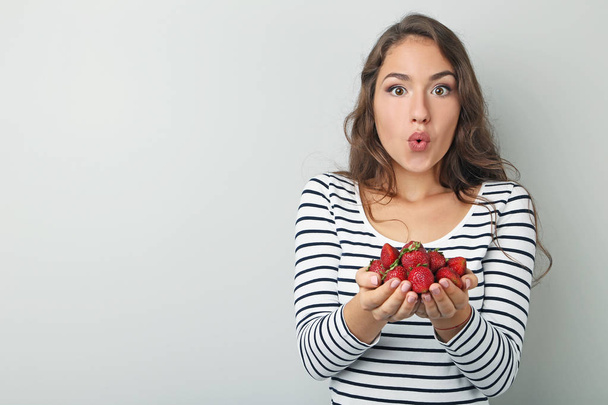 Portrait of young woman with strawberries on grey background - Fotoğraf, Görsel