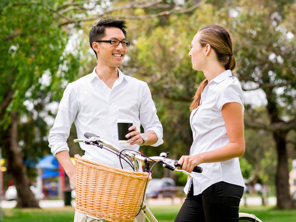 Portrait of smiling couple standing in park with bike talking - Фото, изображение