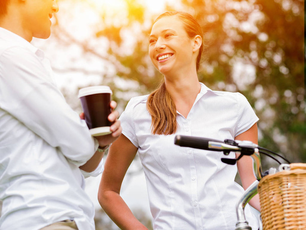 Portret van glimlachen paar staande in park met fiets praten - Foto, afbeelding