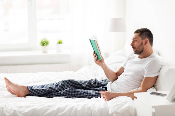 man reading book in bed at home - Foto, afbeelding