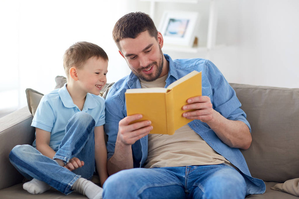 happy father and son reading book sofa at home - Foto, afbeelding