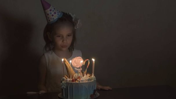la bambina in un cappello festivo soffia candele su una torta di compleanno. Il concetto di compleanno da bambini
. - Foto, immagini
