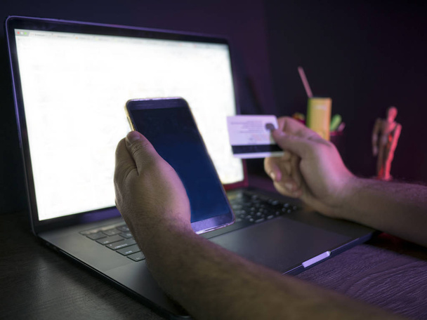 Homme utilisant un ordinateur portable et un téléphone mobile pour faire des achats en ligne et payer par carte de crédit
 - Photo, image