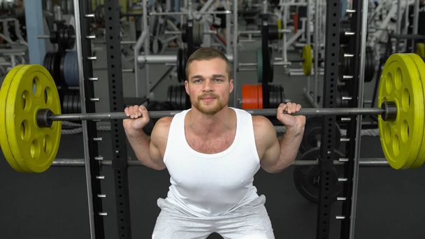 spor salonunda vücut geliştirme. t-shirt giyen bir halter ile ağız kavgası yapıyor. barbell ile egzersiz yaparak vücut geliştirmeci - Fotoğraf, Görsel