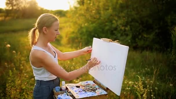 schöne blonde Künstlerin mit einem Pinsel in der Hand zeichnet auf Leinwand in der Natur - Filmmaterial, Video