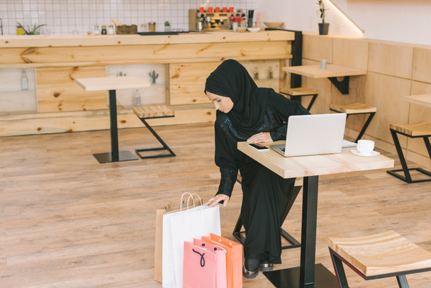 mulher muçulmana olhando para sacos de compras
 - Foto, Imagem