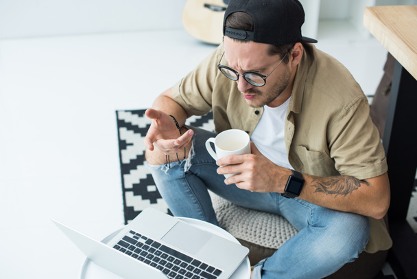 чоловік з чашкою кави дивиться на ноутбук
 - Фото, зображення