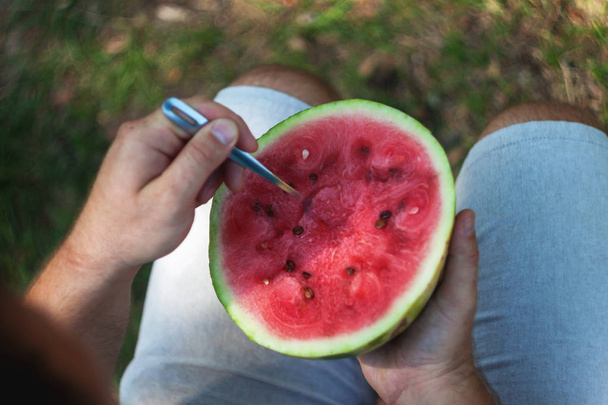 A young man is eating a watermelon with a spoon. The concept of  - Foto, Imagem