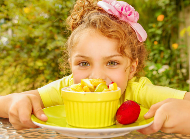 庭の背景に健康的なフルーツ サラダを食べようとして、黄色い t シャツを着ている美しい若い女の子のクローズ アップ - 写真・画像