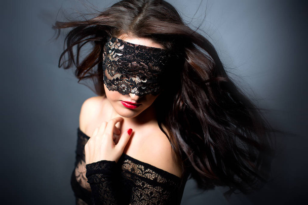 Menina sexy em lingerie preta no fundo preto. Fotocaça erótica encantadora mulher atraente com uma máscara vendada em seu rosto. O cabelo da menina voando no ar
 - Foto, Imagem