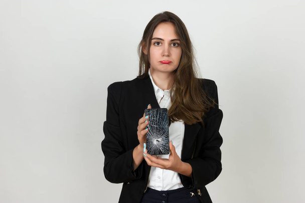 Pretty young businesswoman holding smartphone with broken screen standing over - Photo, Image
