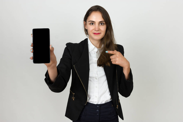 Усміхнена молода бізнес-леді показує порожній екран смартфона і вказує палець на нього
 - Фото, зображення