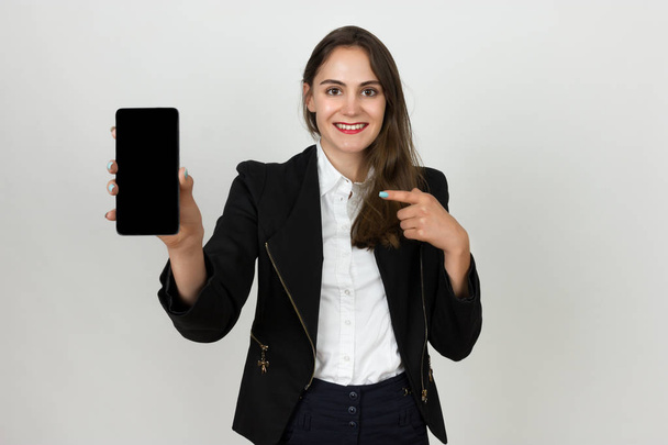 Lächelnde junge Geschäftsfrau zeigt leeren Smartphone-Bildschirm und zeigt mit dem Finger darauf - Foto, Bild