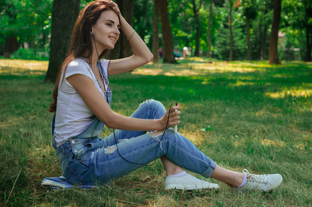 charming pretty girl sitting on the grass in the Park and listens to music - Foto, immagini