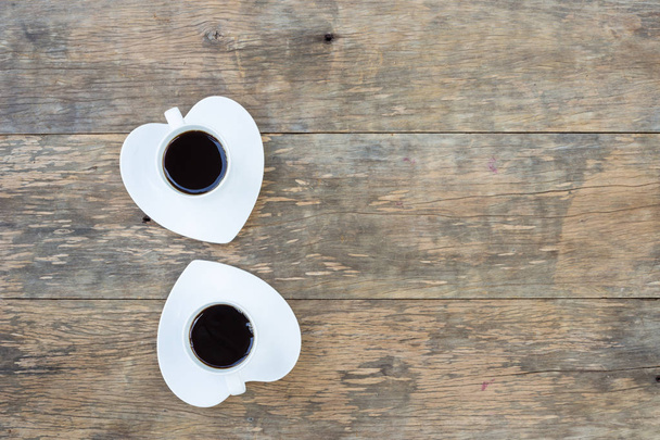 Twee koffie kopjes met hart gevormde schotel op houten achtergrond - Foto, afbeelding