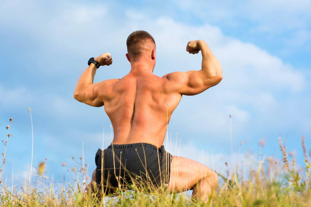 Fisiculturista flexionando os músculos traseiros ao ar livre
 - Foto, Imagem